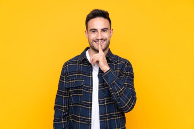 Izole sarı arka plan üzerinde sessizlik jest yapıyor genç yakışıklı adam