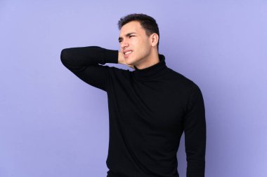 Balıkçı yaka kazaklı, genç, beyaz, yakışıklı bir adam. Mor arka planda, boynu ağrıyan.