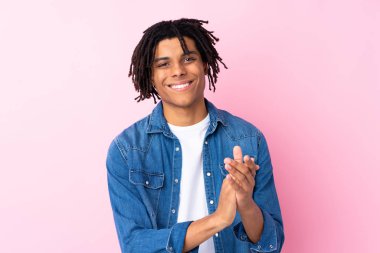 Soyutlanmış pembe arka planda kot gömlekli genç Afrikalı Amerikalı adam alkışlıyor.