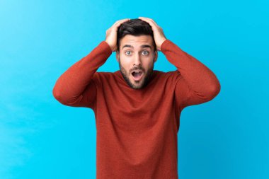 Sakallı, mavi arka planda, yüzünde sürpriz bir ifade olan yakışıklı bir genç.