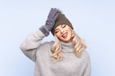 Kışlık şapkalı genç kız mavi arka planda gülüyor.
