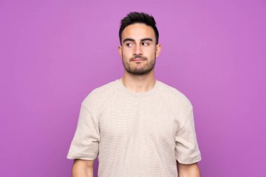 Soyutlanmış mor arka planda genç yakışıklı bir adam şüpheli hareketler yapıyor.