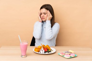 Bej arka planda izole edilmiş, baş ağrısıyla waffle yiyen genç kız.