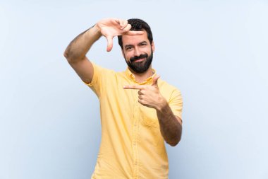 İzole edilmiş mavi arka planda sakallı genç bir adam, odaklanmış bir yüz. Çerçeve sembolü