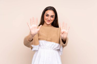 Beyazlı genç bir kadın bej arka planda izole edilmiş dokuz parmaklı sayıyor.