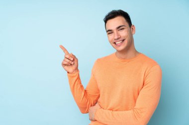 Beyaz tenli yakışıklı adam mavi arka planda izole edilmiş, parmağıyla kenarı gösteriyor.