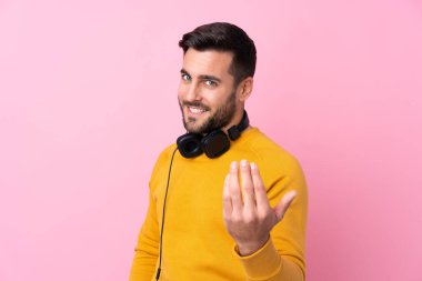 Soyutlanmış pembe arka planda kulaklıkları olan yakışıklı genç bir adam, bizimle gelmesi için davet ediyor. Gelmene sevindim.