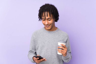 Mor arka planda izole edilmiş genç Afro-Amerikan bir adam elinde kahve ve bir cep telefonu tutuyordu.
