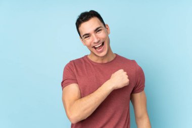 Mavi arka planda izole edilmiş beyaz yakışıklı bir adam zaferi kutluyor.