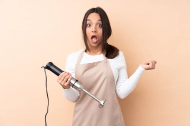 Genç esmer kız, el blendırı kullanıyor. İzole edilmiş arka planda, şaşırmış yüz ifadesi var.