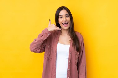 Genç esmer kadın izole edilmiş sarı arka planda telefon jesti yapıyor. Bana geri dönüş işareti ver.