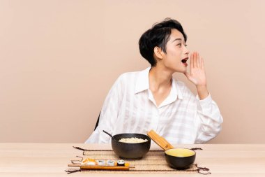 Genç Asyalı bir kız bir kase erişte ve sushi ile ağzı açık bağırıyor.