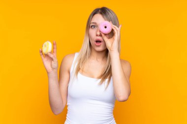 Sarışın bir kadın mavi arka planda gözünün içinde donut tutuyor.