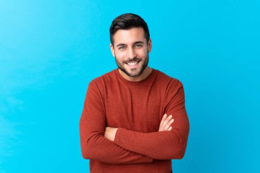 Sakallı, genç ve yakışıklı bir adam mavi arka planda gülüyor.