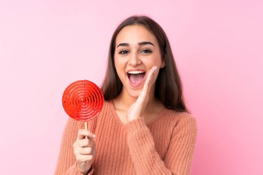 Pembe arka planda lolipop tutan genç bir kız ağzı açık bağırıyor.