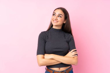 Soyutlanmış pembe arka planda genç bir kız gülümserken yukarı bakıyor