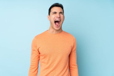 Beyaz tenli yakışıklı adam mavi arka planda izole edilmiş ve ağzı açık bağırıyor.