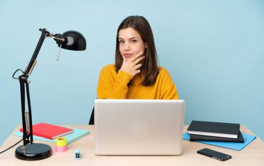 Öğrenci kız, mavi arka planda izole bir şekilde evinde ders çalışıyor.