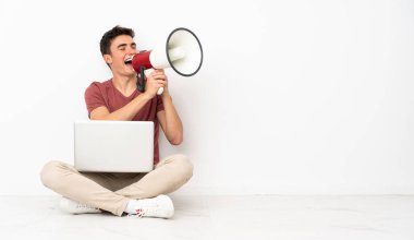 Flor 'da dizüstü bilgisayarıyla oturan genç adam megafonla bağırıyor.