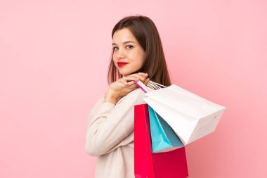 Pembe arka planda izole edilmiş genç bir kız alışveriş torbaları tutuyor ve gülümsüyor.