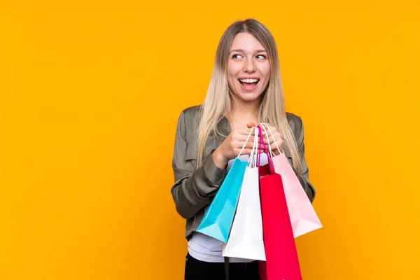 Young Blonde Woman Isolated Yellow Background Holding Shopping Bags Surprised — 스톡 사진