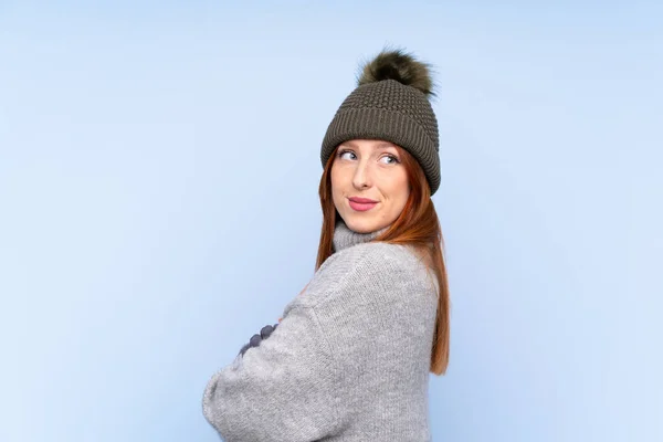 若いですRedheadロシア人女性とともに冬の帽子以上隔離された青の背景笑い — ストック写真