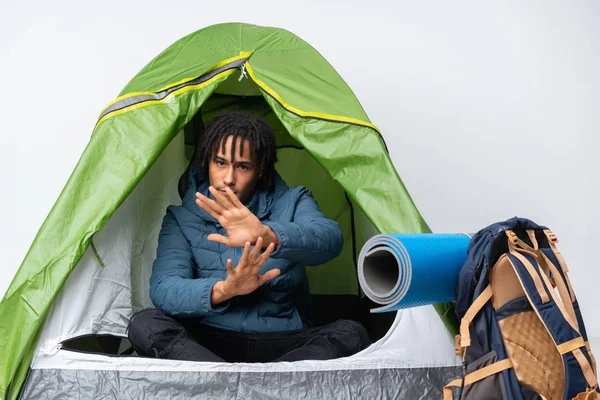 Young african american man inside a camping green tent nervous stretching hands to the front