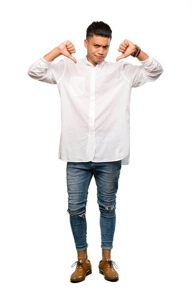 A full-length shot of a Young man showing thumb down over isolated white background