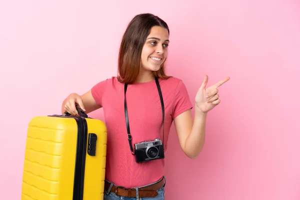 Teenager Cestovatel Dívka Drží Kufr Přes Izolované Růžové Pozadí Ukazuje — Stock fotografie