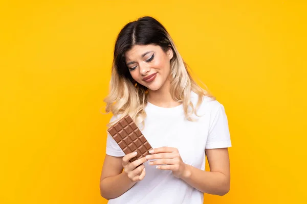 Teenager Dívka Izolované Žlutém Pozadí Čokoládovou Tabletu Mají Pochybnosti — Stock fotografie