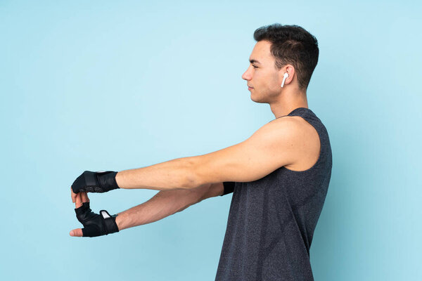 Young sport man over isolated on blue background stretching arm