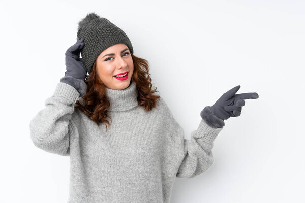 Young Russian woman with winter hat over isolated white background surprised and pointing finger to the side