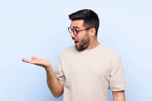 Jovem Homem Bonito Com Barba Sobre Fundo Azul Isolado Segurando — Fotografia de Stock