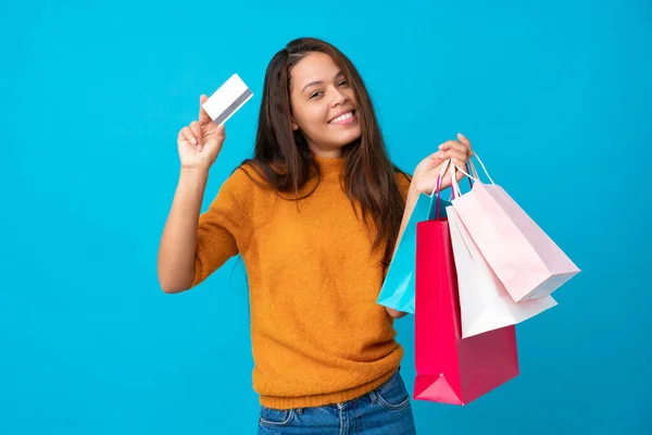 若いですブラジルの女の子以上隔離された青の背景保持ショッピングバッグとクレジットカード — ストック写真
