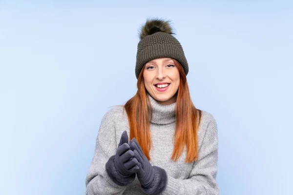 若いですRedheadロシア人女性とともに冬の帽子以上隔離された青の背景拍手 — ストック写真