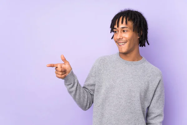 紫色の背景に指を向けて製品を提示する若いアフリカ系アメリカ人の男性 — ストック写真