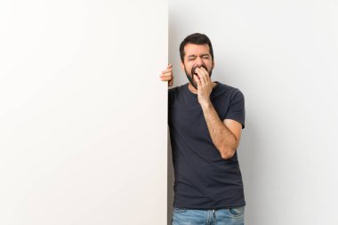 Sakallı, kocaman boş bir levha tutan, esneyen ve ağzı açık olan genç yakışıklı bir adam.