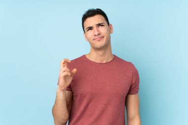 Beyaz tenli yakışıklı adam mavi arka planda izole edilmiş, şans diliyor ve en iyisini diliyor.