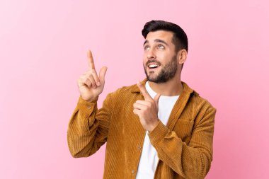 Pembe arka planda kadife ceket giyen sakallı yakışıklı genç adam işaret parmağıyla işaret etmek harika bir fikir.