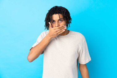 İzole edilmiş mavi arka planda ağzı elleriyle kapatan genç bir Afro-Amerikalı.