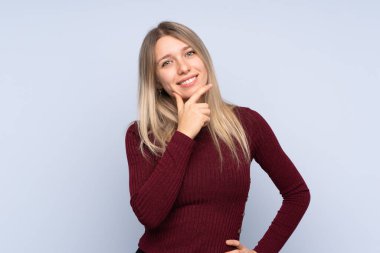 İzole edilmiş mavi arka planda gülümseyen genç sarışın kadın.