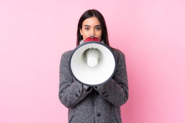 Soyutlanmış pembe arka planda genç esmer kadın megafondan bağırıyor.