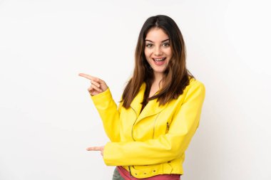 Beyaz arka planda izole edilmiş genç beyaz kadın şaşırmış ve işaret ediyor.