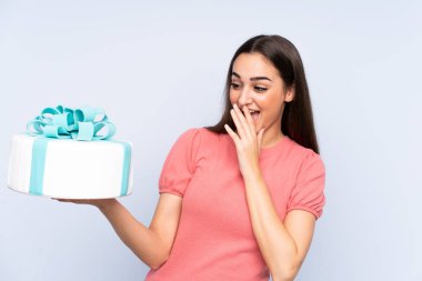 Pasta şefi elinde büyük bir pasta tutuyor. Mavi arka planda, şaşırmış ve şok olmuş bir yüz ifadesi var.