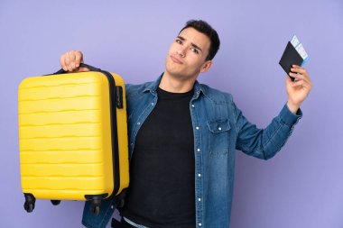 Beyaz tenli yakışıklı, mor arka planda izole edilmiş, bavullu ve pasaportlu mutsuz bir genç.