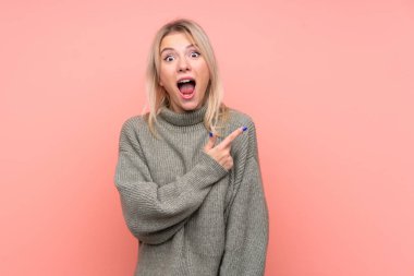 Soyutlanmış pembe arka planda genç sarışın kadın şaşırmış ve işaret ediyor.