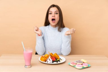 Bej arka planda yalıtılmış waffle yiyen genç kız şaşırmış yüz ifadesi ile