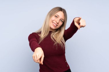 İzole edilmiş mavi arka plandaki genç sarışın kadın gülümserken seni işaret ediyor.