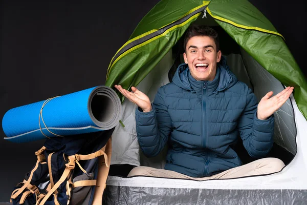 Teenager caucasian man inside a camping green tent isolated on black background with shocked facial expression