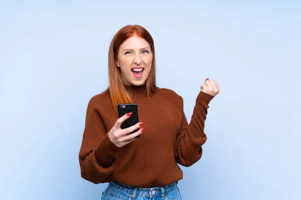Young Redhead Woman Isolated Blue Background Phone Victory Position — Stock Photo, Image